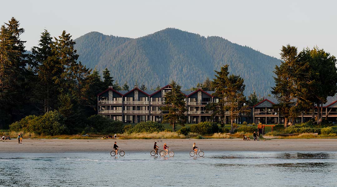 Exterior of hotel with people riding bikes on the beach Exterior of hotel with people riding bikes on the beach