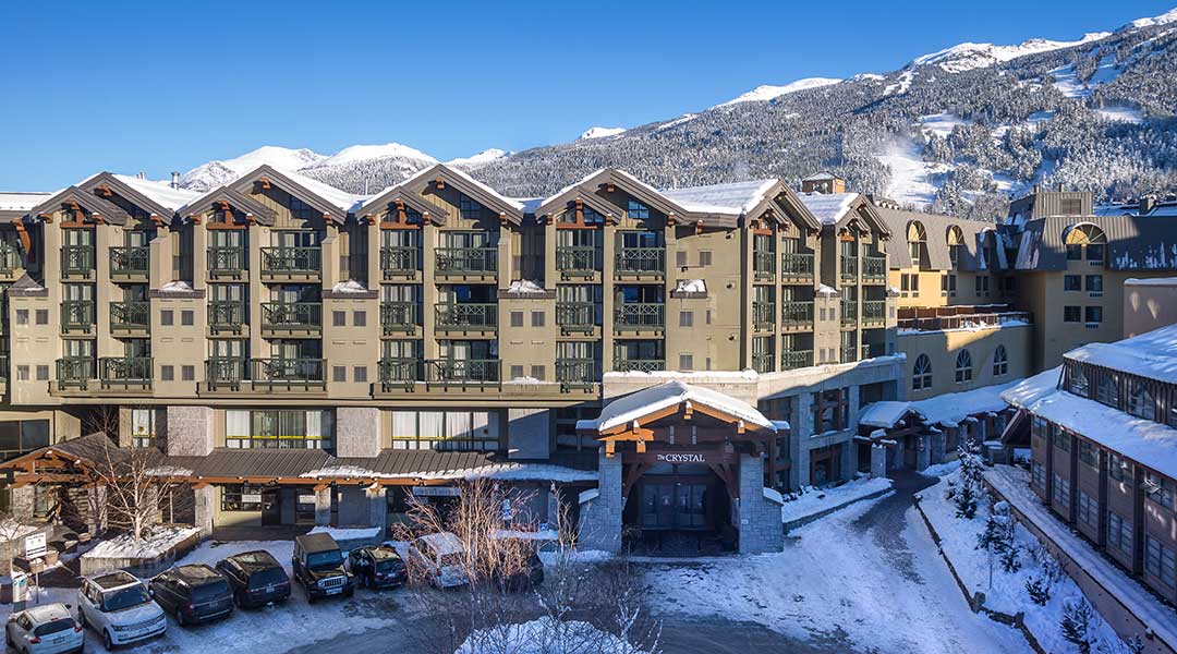 An aerial view of the exterior entrance and building to the Crystal Lodge and Suites in Whistler Village during winter An aerial view of the exterior entrance and building to the Crystal Lodge and Suites in Whistler Village during winter