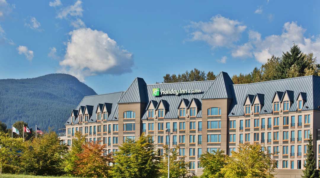 The exterior building of the Holiday Inn and Suites North Vancouver near the mountains The exterior building of the Holiday Inn and Suites North Vancouver near the mountains