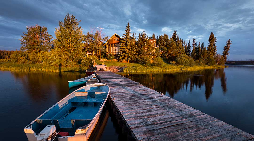 A boat next to a wooden dock that leads towards the exterior building of the Eagles Nest Resort in Anahim Lake Northern BC A boat next to a wooden dock that leads towards the exterior building of the Eagles Nest Resort in Anahim Lake Northern BC