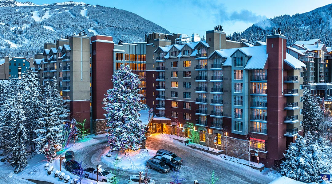 The exterior building and parking lot of the Hilton Whistler Resort and Spa during the winter in the Coast Mountains