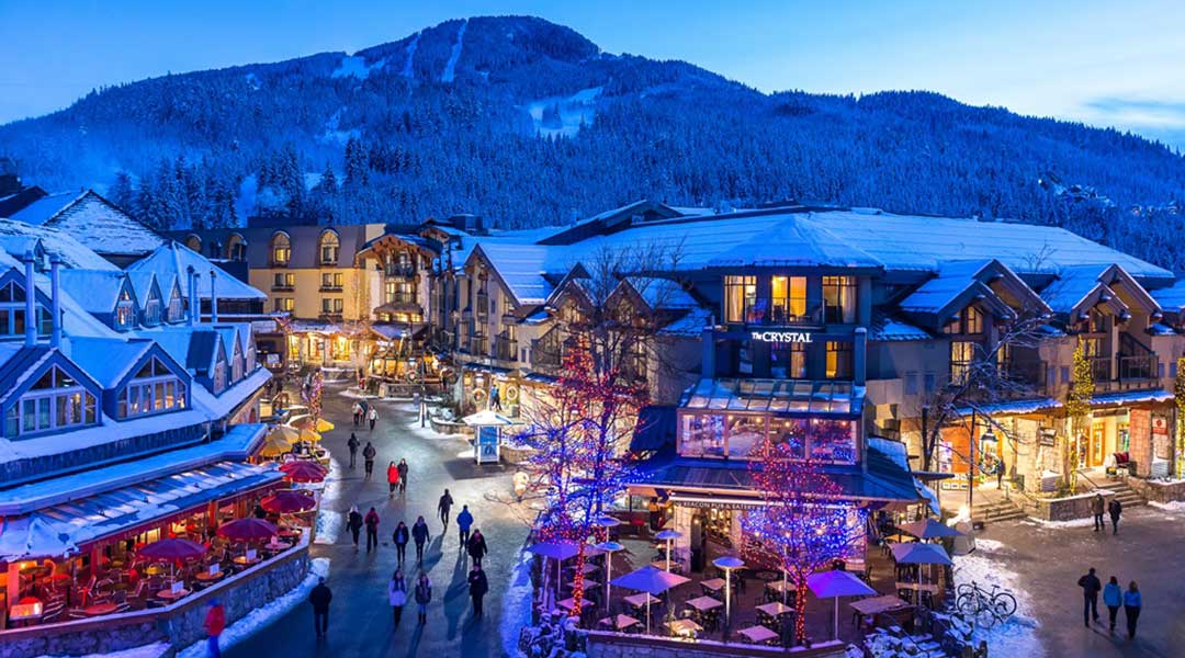 An aerial view of the exterior entrance and building to the Crystal Lodge and Suites in Whistler Village during winter and in the evening An aerial view of the exterior entrance and building to the Crystal Lodge and Suites in Whistler Village during winter and in the evening