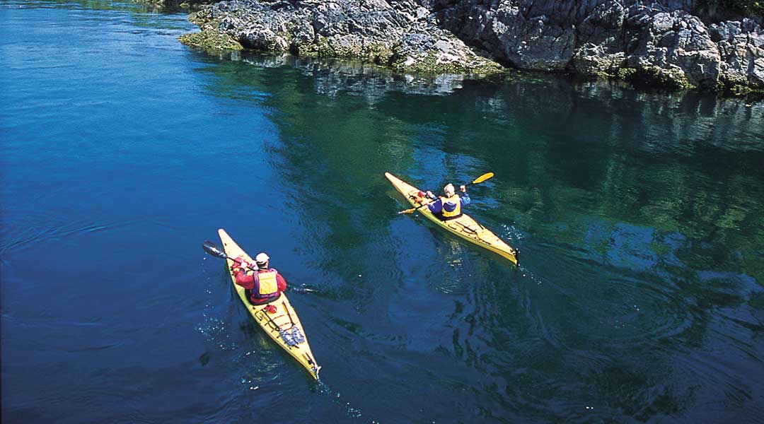 Two kayakers kayaking next to rocky bluffs near the Brentwood Bay Resort and Spa on Vancouver Island Two kayakers kayaking next to rocky bluffs near the Brentwood Bay Resort and Spa on Vancouver Island